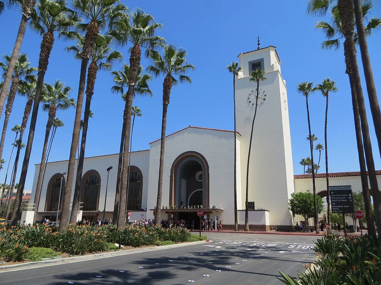Union Station de Los Angeles, prédio branco com torre do relógio e palmeiras na frente, sob céu azul.