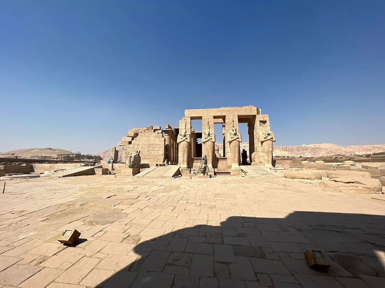 Ruínas do Ramesseum, em Luxor, com colunas e estátuas osiríacas de pé sobre a areia.