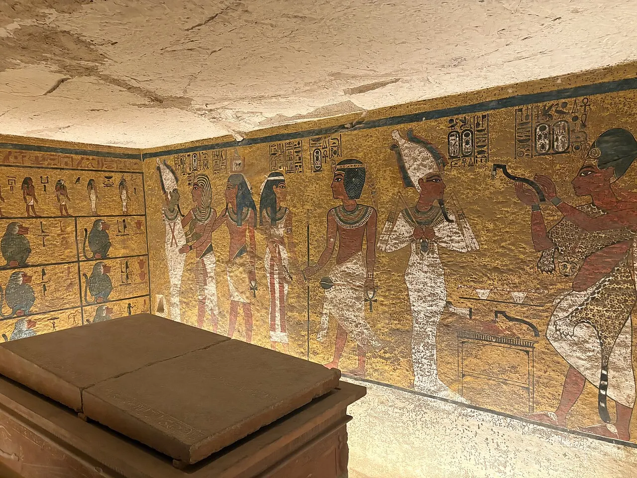 Câmara pintada de uma tumba no Vale dos Reis, com figuras nas paredes amarelas e um sarcófago de pedra.