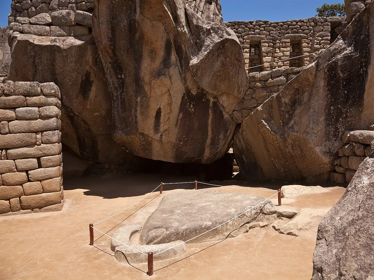 Templo do Condor em Machu Picchu, com as rochas altas e a pedra no chão cercada por uma corda.