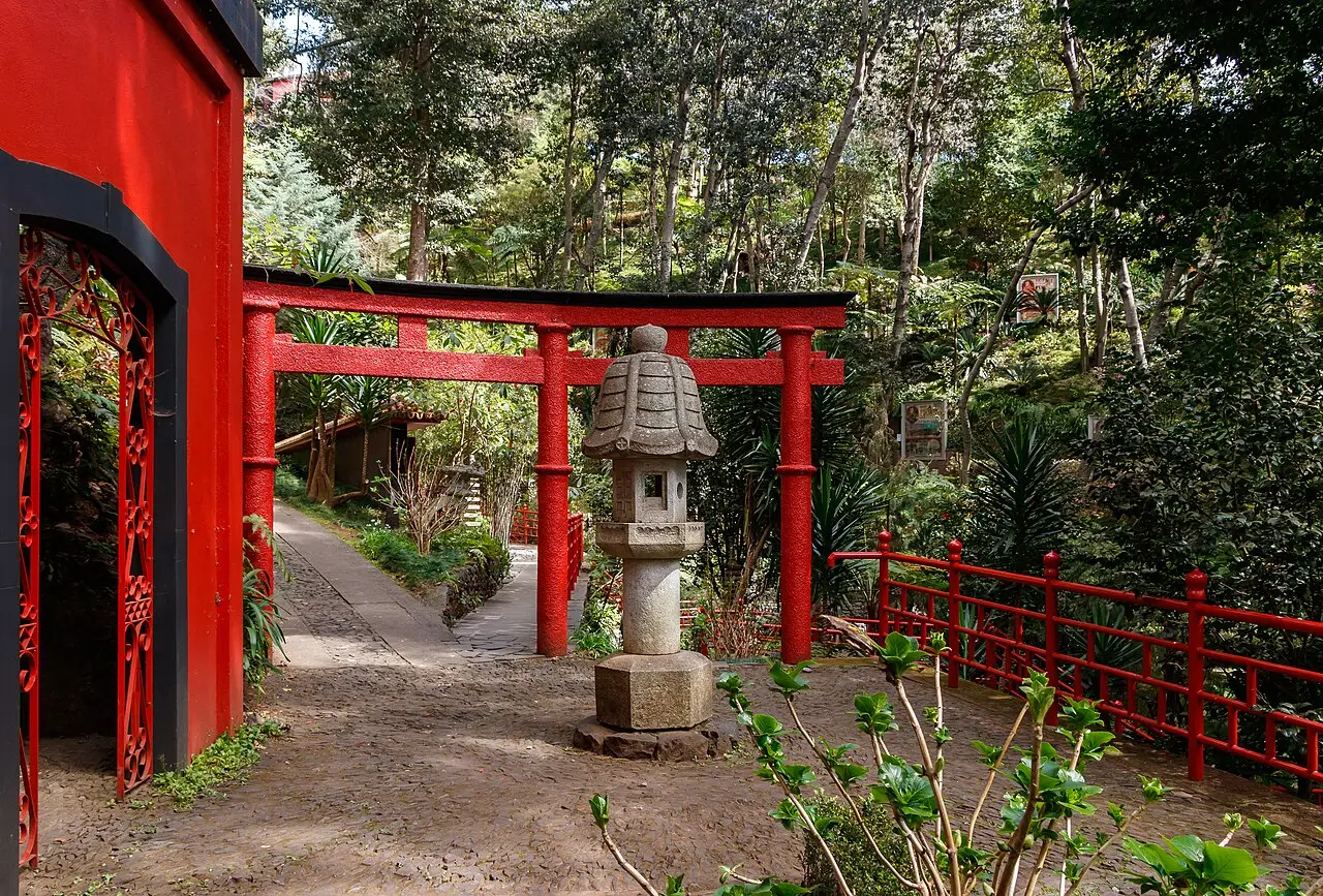 O jardim oriental do Monte Palace, com portais e cercas vermelhas, uma lanterna de pedra e plantas tropicais à sombra das árvores.