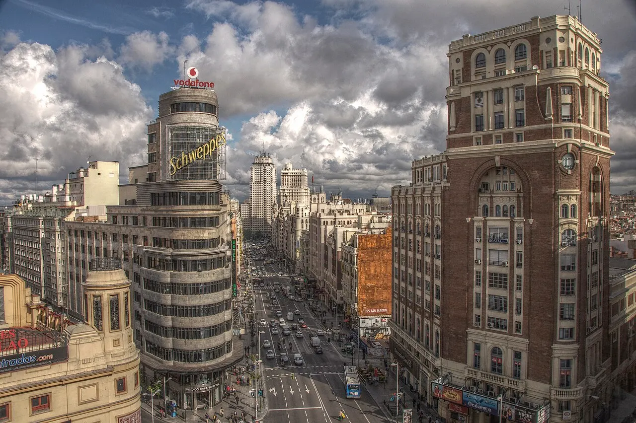 Gran Vía vista de cima, com o prédio curvo do letreiro Schweppes, carros na avenida e a torre de tijolo à direita.