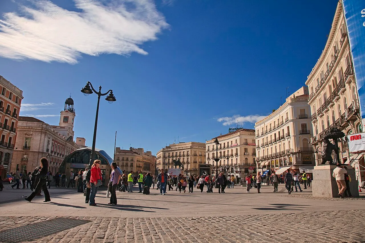 Puerta del Sol, com os prédios curvos, a estátua do urso à direita e a torre do relógio ao fundo.