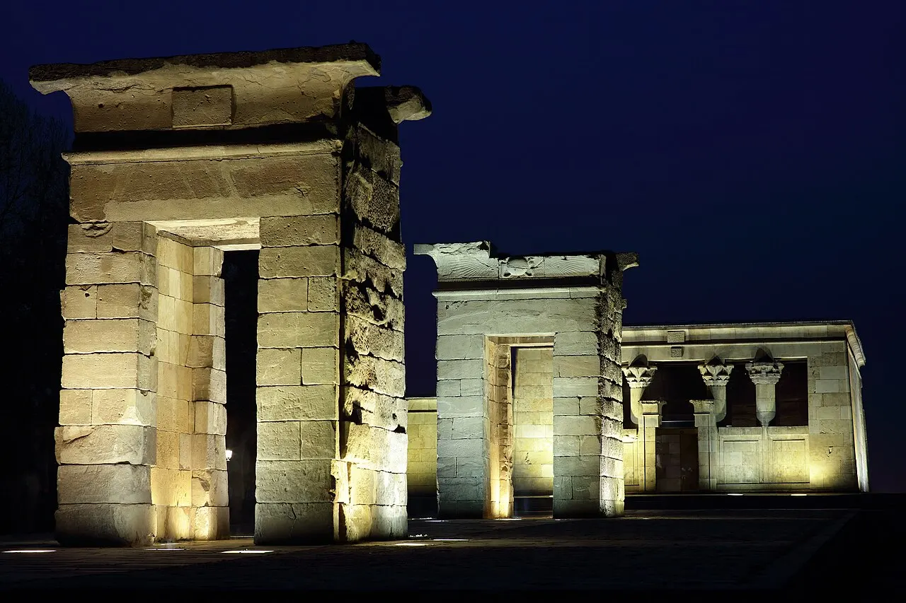 Portais de pedra e santuário do Templo de Debod, em Madri, iluminados à noite contra o céu escuro.