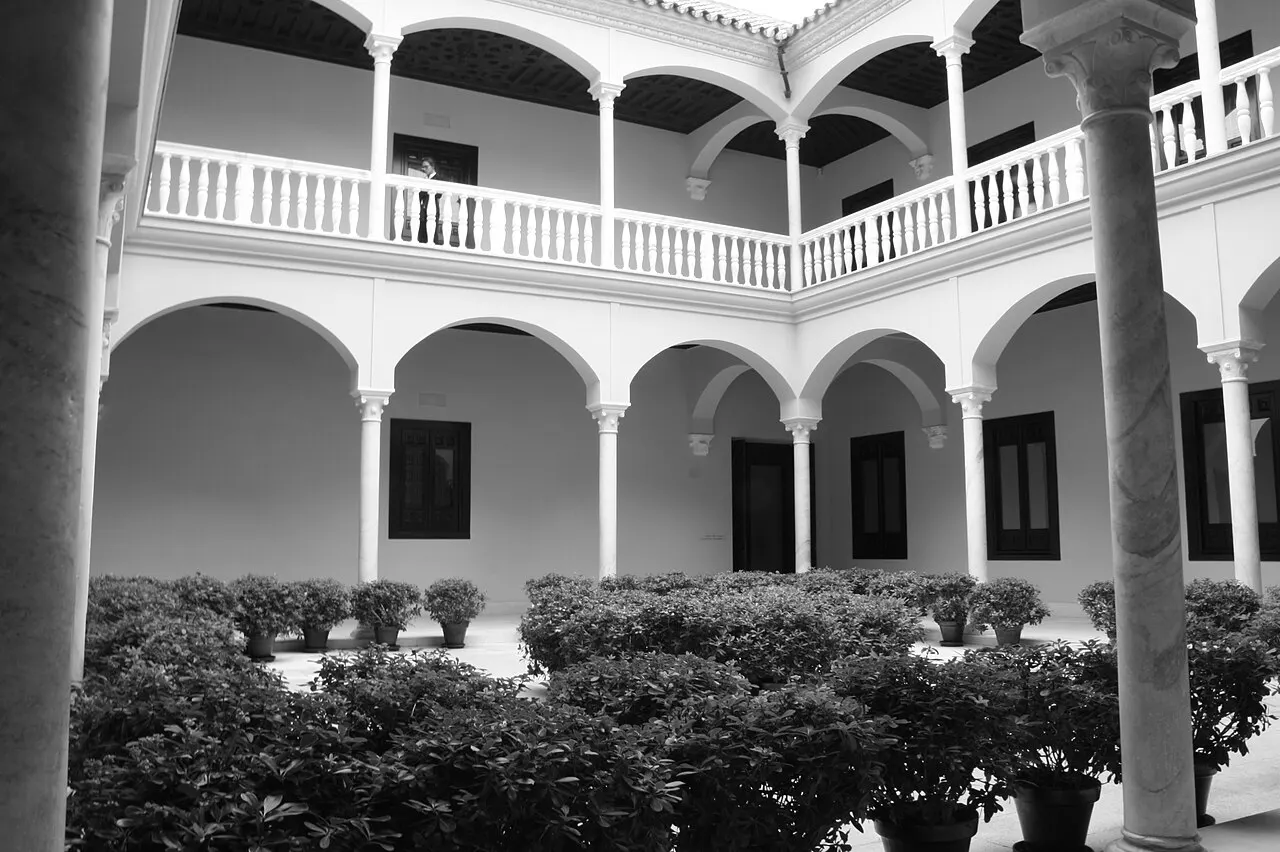 La cour à arcades blanches du palais de Buenavista, avec une galerie à balustrade et des plantes en pot, en photo noir et blanc.