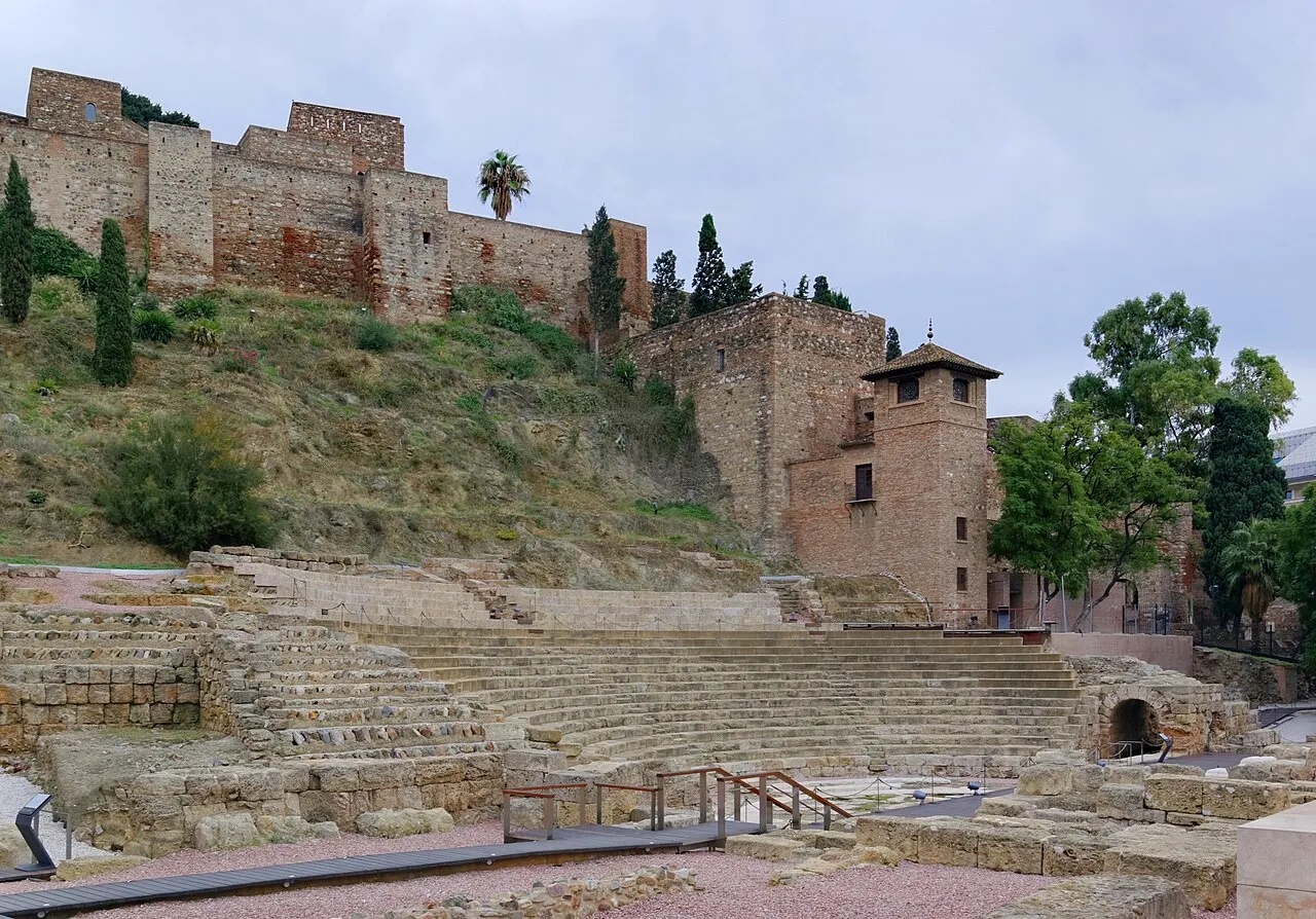 As arquibancadas de pedra do Teatro Romano de Málaga, com a muralha e as torres da Alcazaba na encosta logo acima.