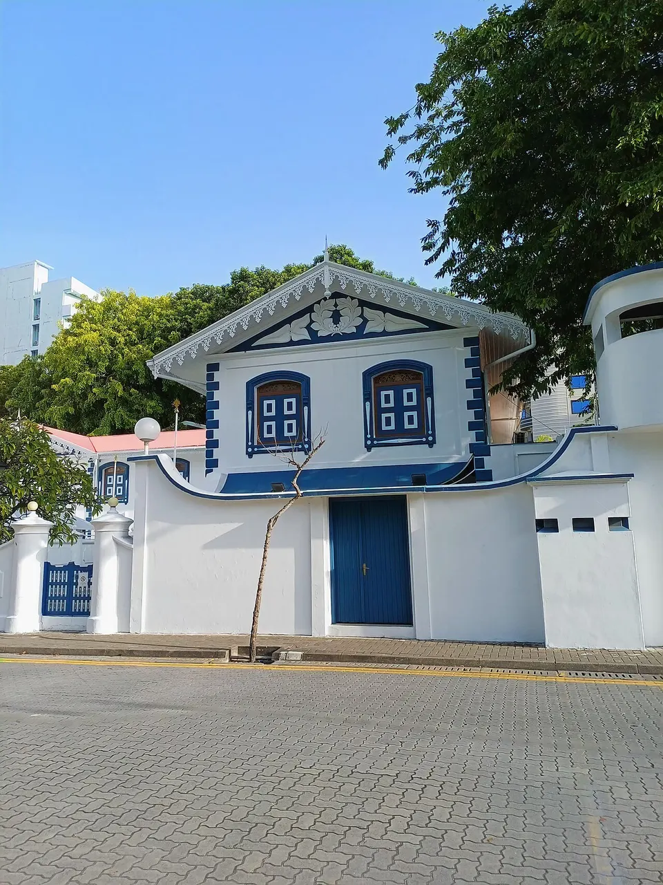 O Medhu Ziyaaraiy, um santuário pequeno de paredes brancas com detalhes azuis e frontão recortado, numa rua calçada de Malé.