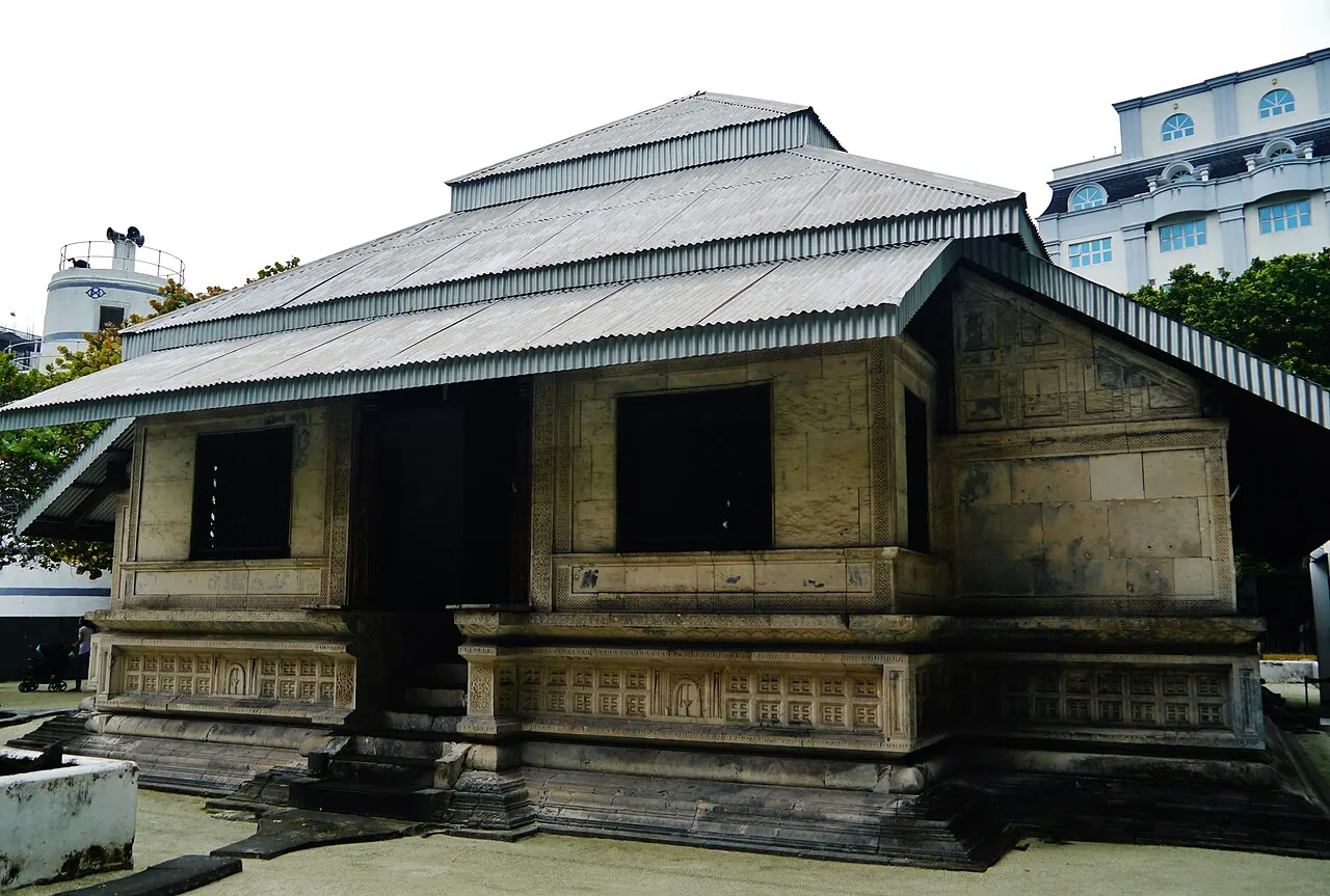 A Hukuru Miskiy, em Malé, uma mesquita baixa de pedra de coral escura com friso entalhado e telhado de chapa em duas águas.