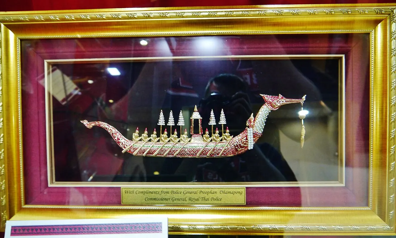 Uma vitrine do Museu Nacional das Maldivas com o modelo dourado de uma embarcação real com remadores, numa moldura vermelha e dourada.