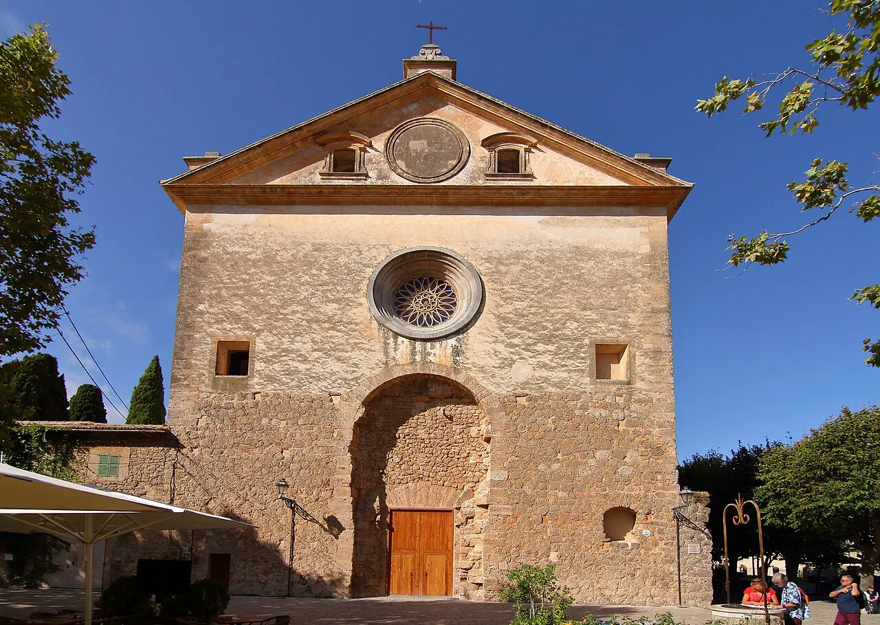 A fachada de pedra da igreja da Cartuxa de Valldemossa, com rosácea, frontão triangular e uma porta de madeira sob o arco.