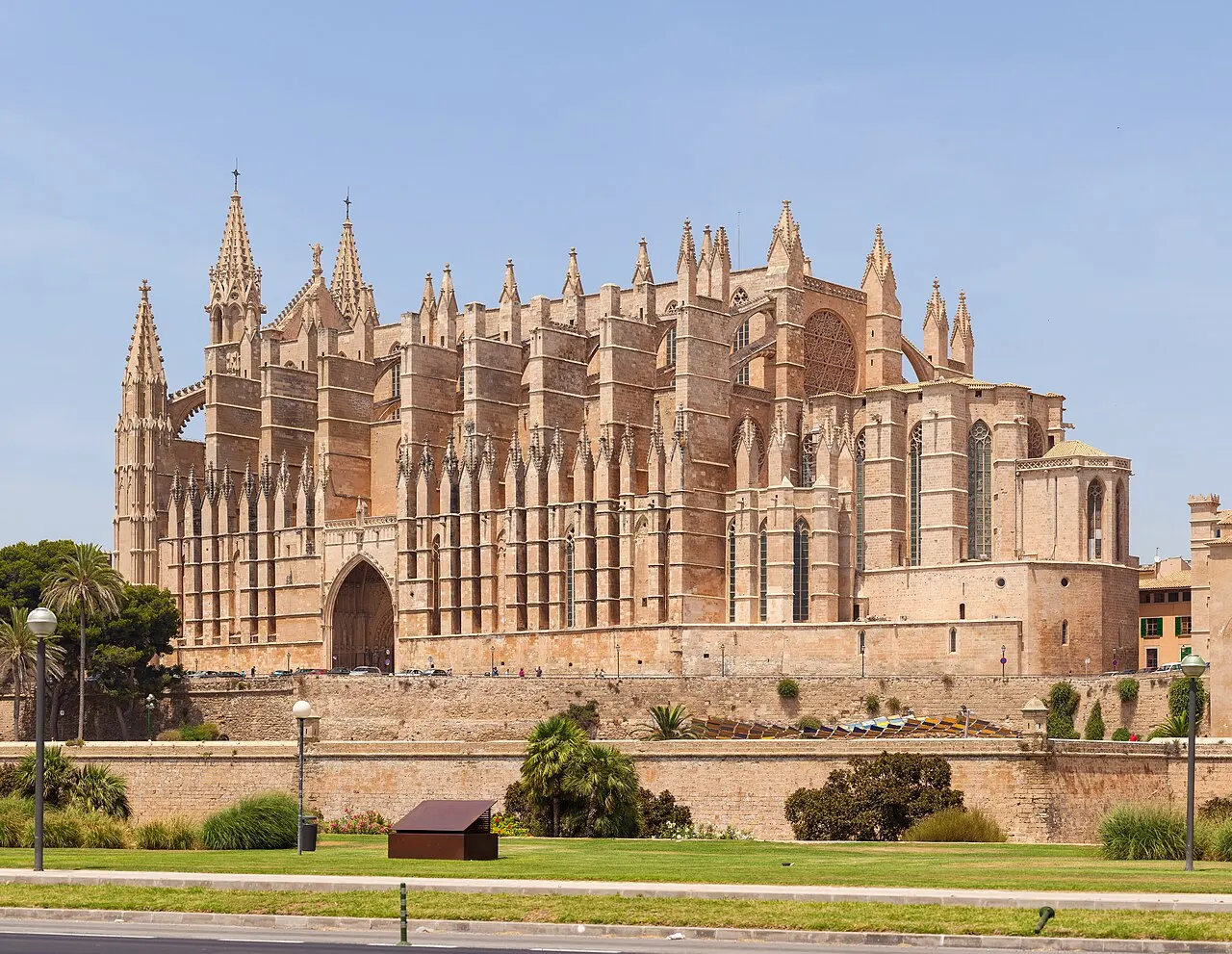 A Catedral gótica de Palma, de pedra dourada, com os contrafortes e pináculos, vista por cima do muro e do gramado da orla.