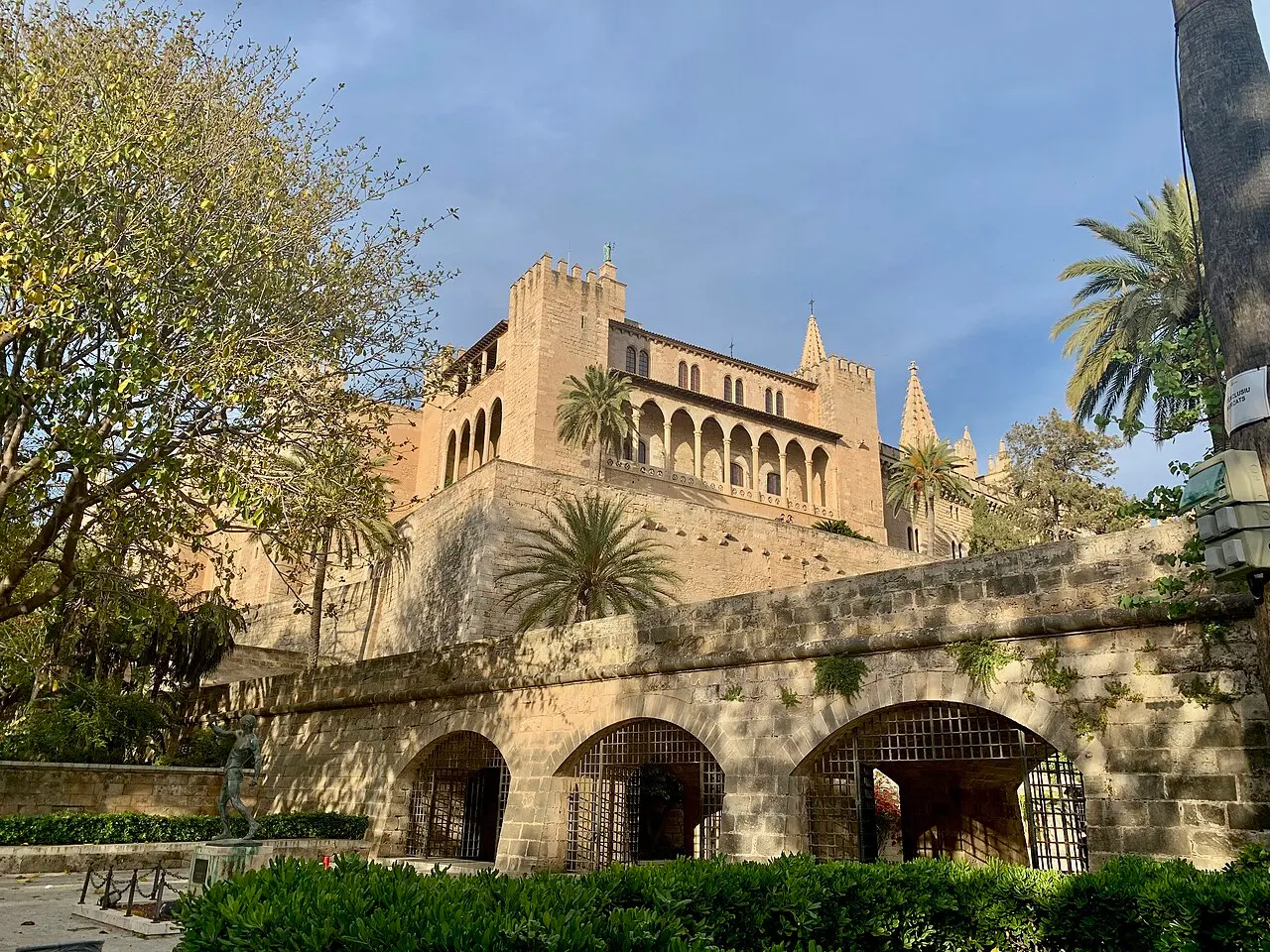 O Palácio Real da Almudaina visto do jardim do Hort del Rei, com a muralha de arcos, palmeiras e as torres da catedral atrás.