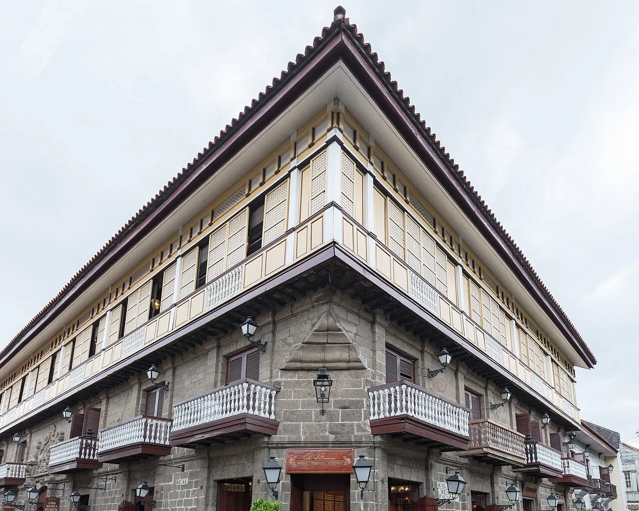 Fachada de esquina da Casa Manila, com balcões de madeira e janelas de veneziana sobre o térreo de pedra.