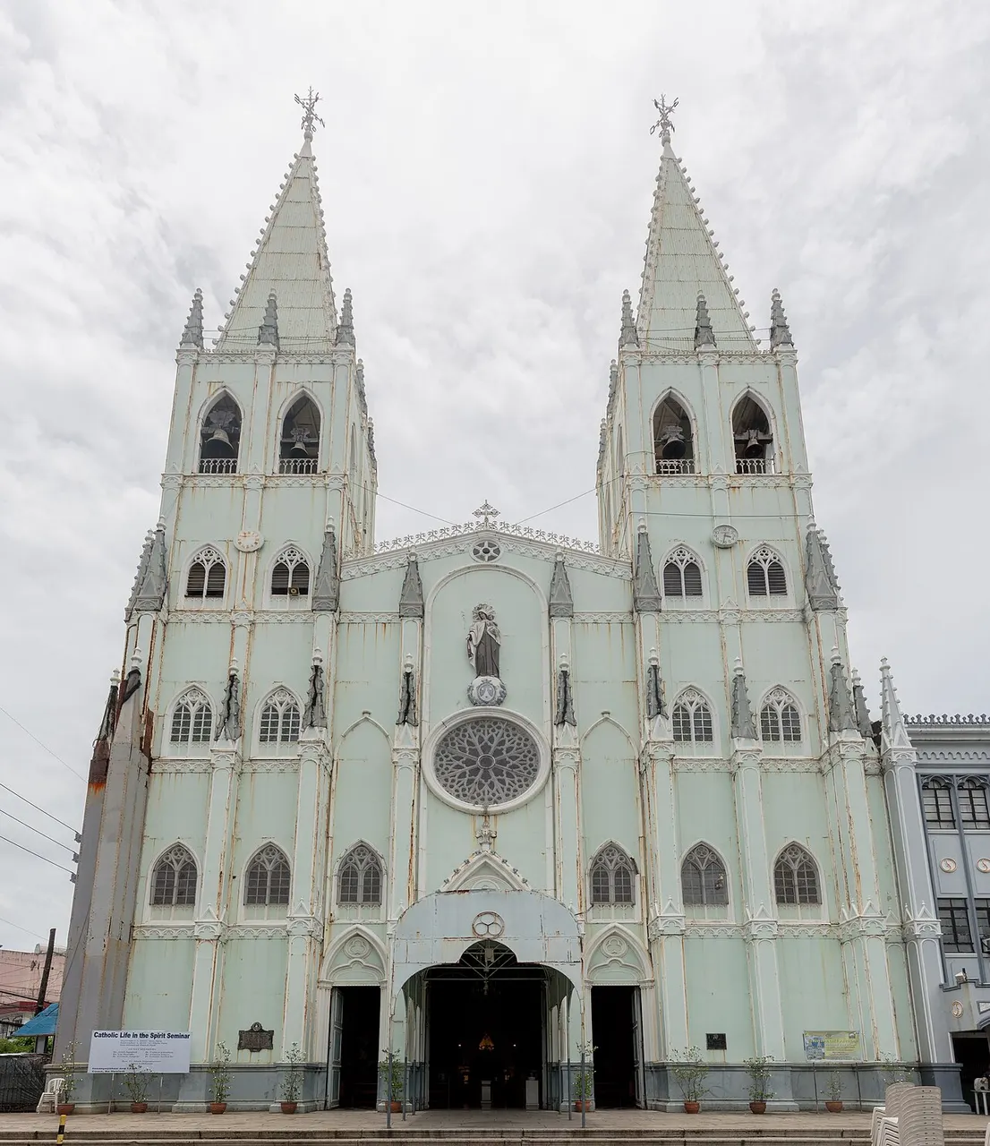 Fachada cinza de igreja neogótica com duas torres pontiagudas iguais lado a lado.