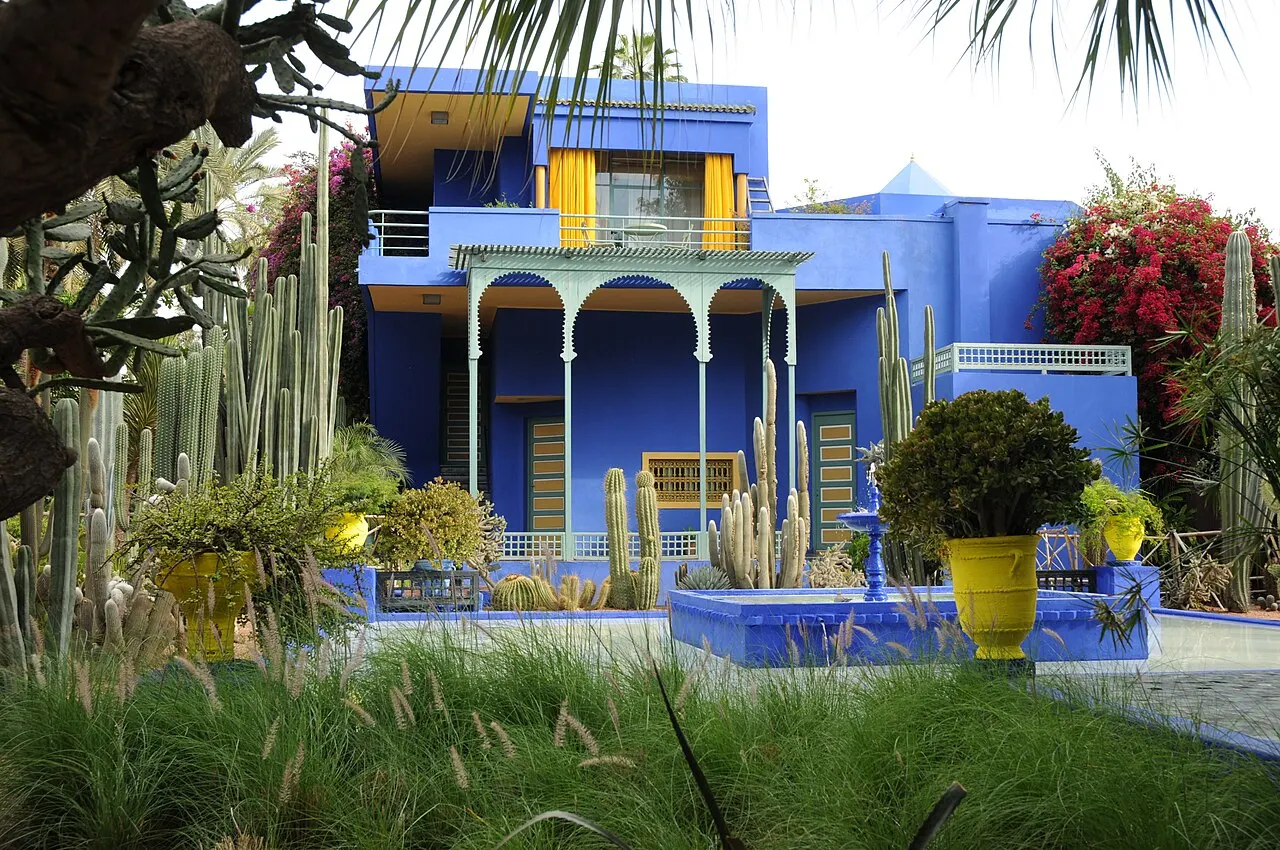 Villa azul do Jardim Majorelle, em Marraquexe, com colunas e vasos amarelos, entre plantas.