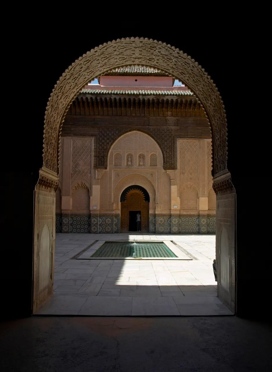 Arco esculpido em cedro e estuque no pátio da Medersa Ben Youssef, em Marraquexe, com o tanque ao fundo.