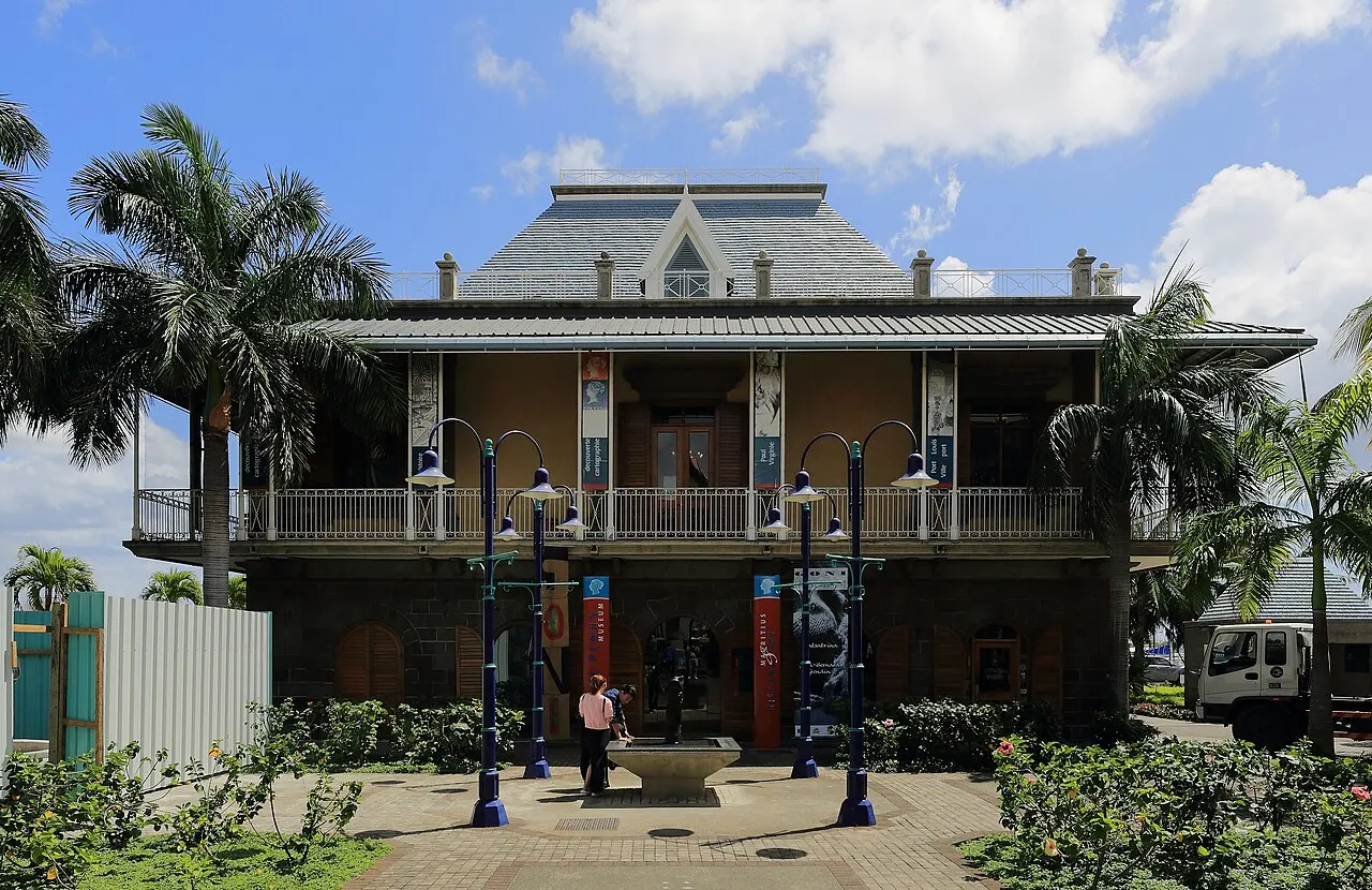 O prédio de estilo colonial do Blue Penny Museum, com varandas e telhado cinza, entre palmeiras na orla de Port Louis.