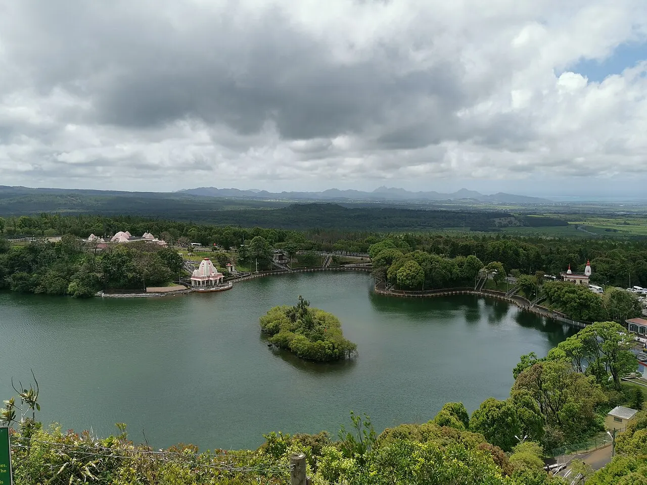 O lago de cratera de Ganga Talao visto do alto, de água verde-escura com uma ilhota de mata e templos pequenos na margem.