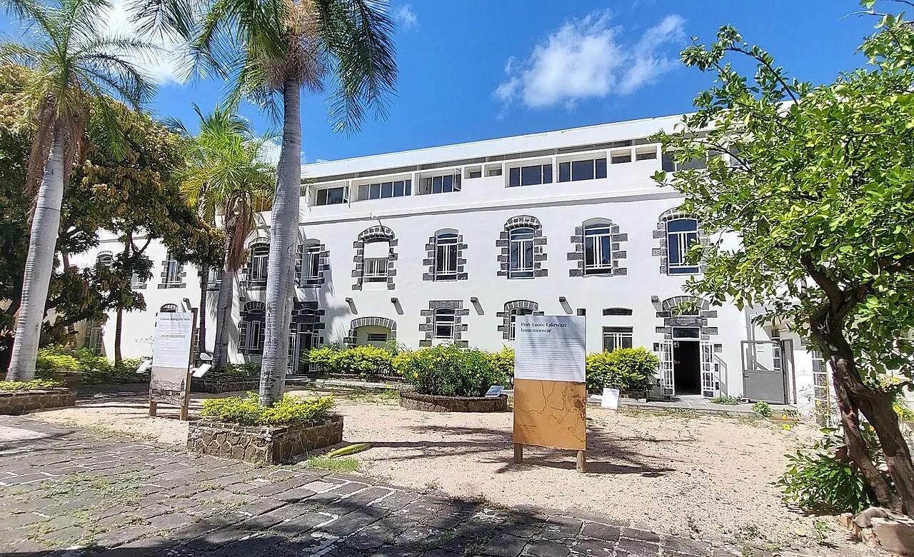 O prédio branco de dois andares do antigo hospital militar de Port Louis, sede do Intercontinental Slavery Museum, entre palmeiras.
