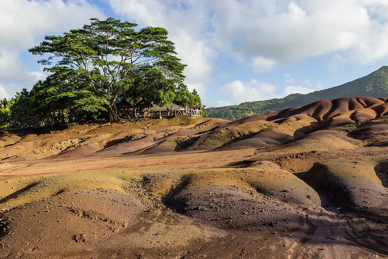 As ondulações de terra em tons de vermelho, ocre e violeta da Terra das Sete Cores, em Chamarel, com árvores ao fundo.