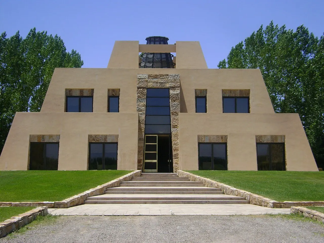 O prédio da Bodega Catena Zapata, de paredes cor de areia em degraus no formato de uma pirâmide, com uma escadaria central, gramado na frente e árvores dos lados.