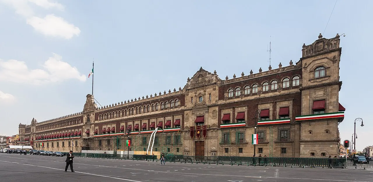 Fachada longa do Palacio Nacional, na Cidade do México, de pedra vermelha, vista do Zócalo.