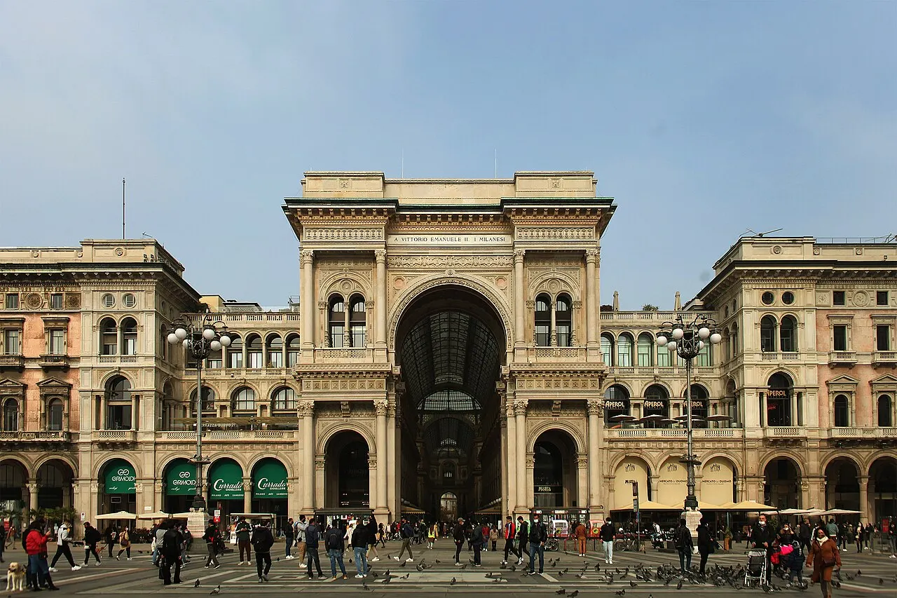 Entrada em arco da Galleria Vittorio Emanuele II, vista da Piazza del Duomo, com pessoas circulando à frente.
