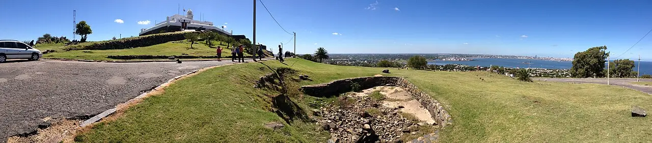 Colina do Cerro de Montevidéu, com a fortaleza no topo, o gramado em primeiro plano e a baía à direita.