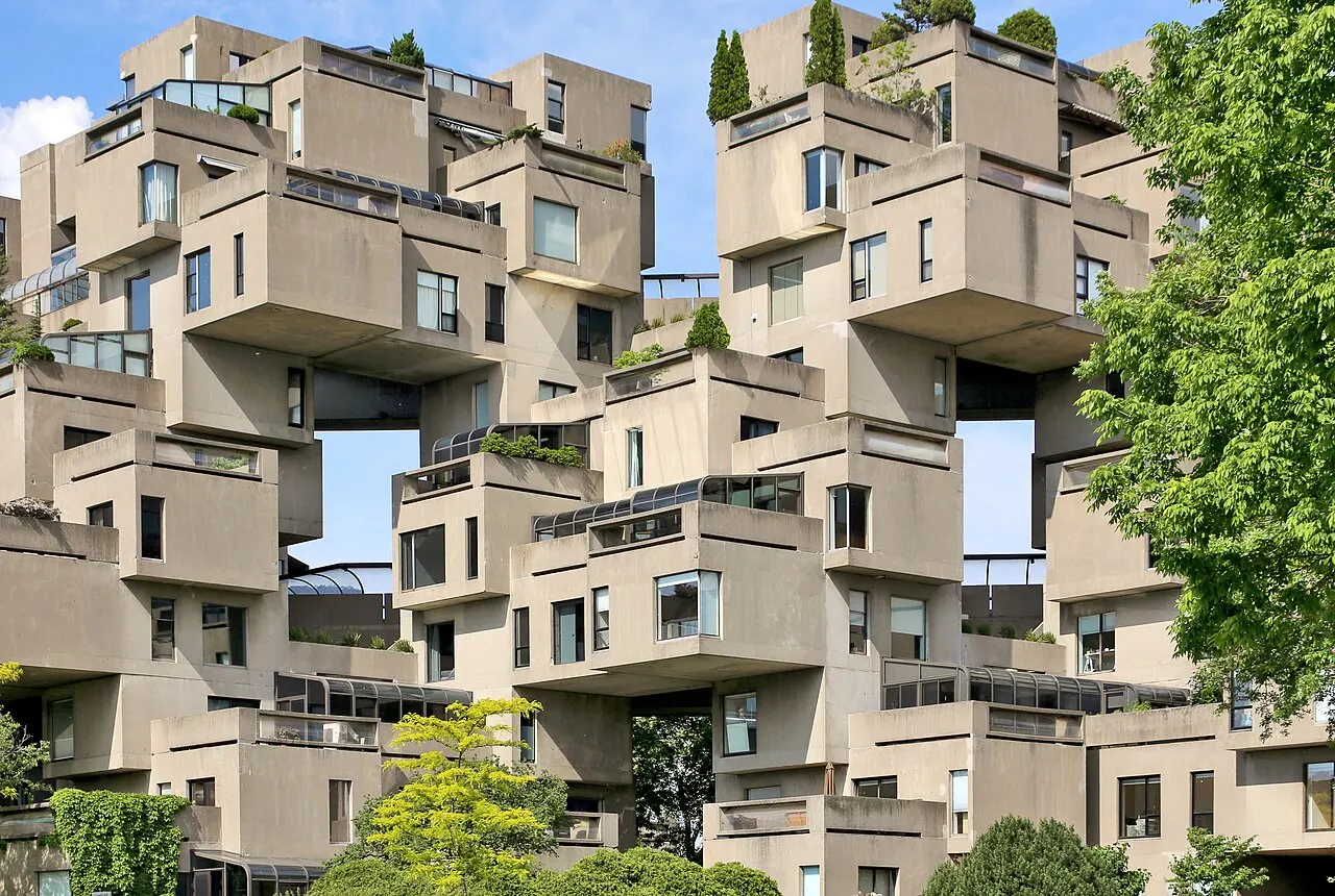 Os blocos de concreto empilhados do Habitat 67, com vegetação em volta e céu azul ao fundo.