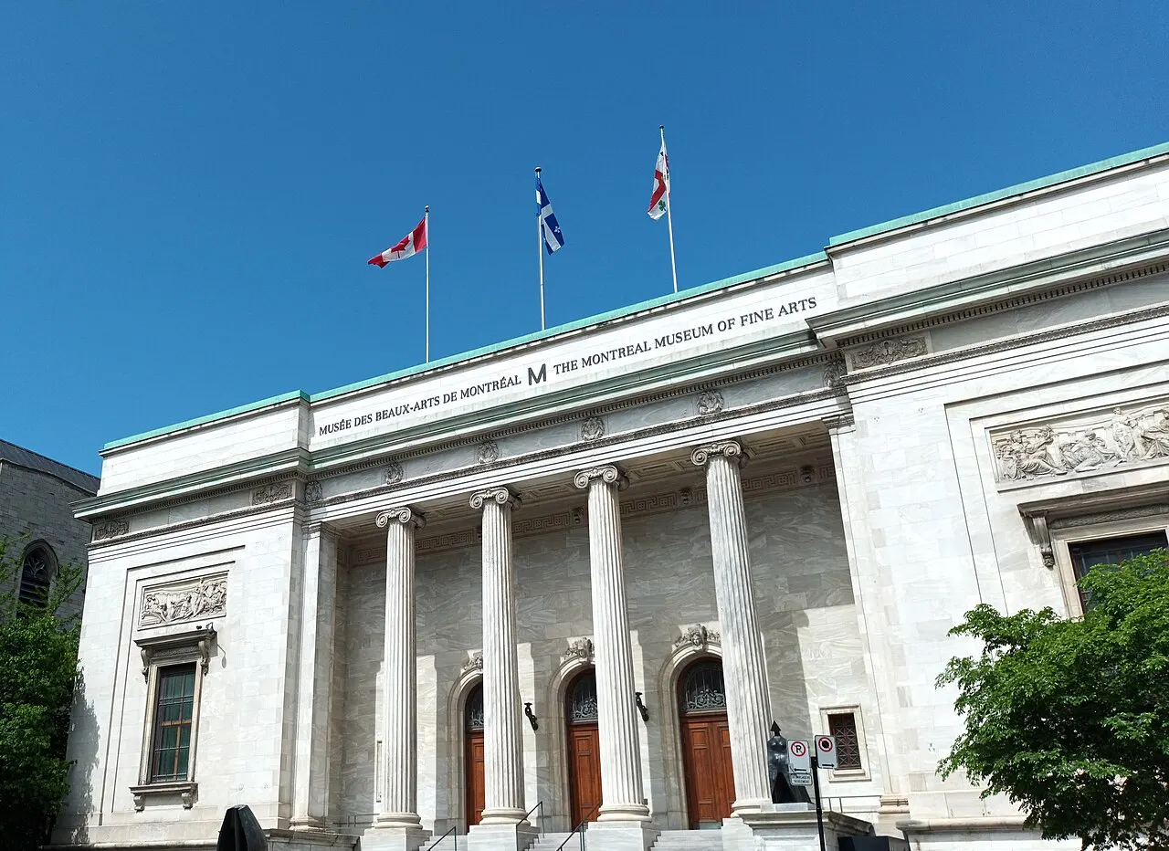 Prédio de colunas brancas do Museu de Belas-Artes de Montreal, com bandeiras no topo, sob céu azul.