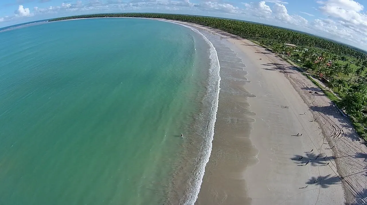 A Praia de Garapuá vista do alto, com a areia em curva entre o mar verde-claro e a mata.