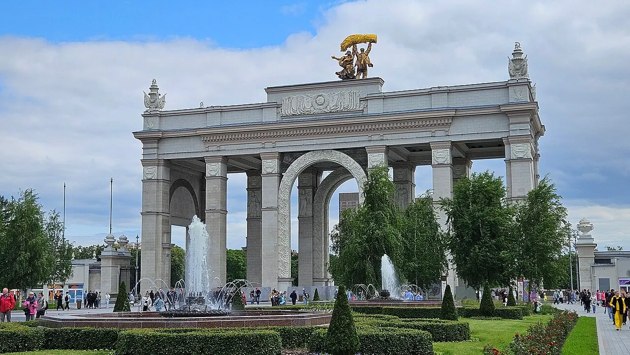 L'arc de l'entrée principale de VDNKh, à Moscou, surmonté d'une sculpture, avec des arbres et des fontaines devant.
