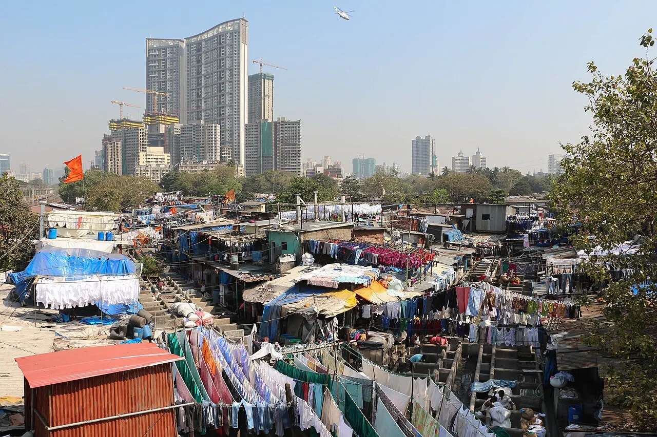 A lavanderia ao ar livre Dhobi Ghat, com varais e tanques, e torres de apartamentos ao fundo.
