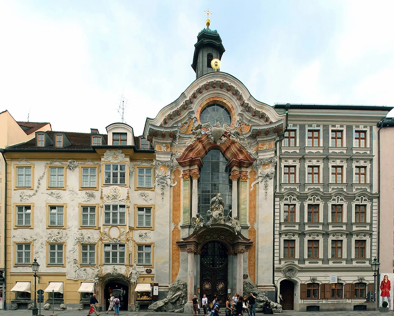 Fachada barroca da Asamkirche, encaixada entre as casas da rua, com uma pequena torre no alto.