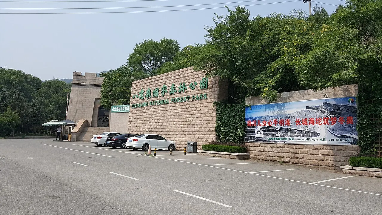 Entrada do Parque Florestal Nacional de Badaling, com portal de pedra, letreiro e estacionamento em primeiro plano.