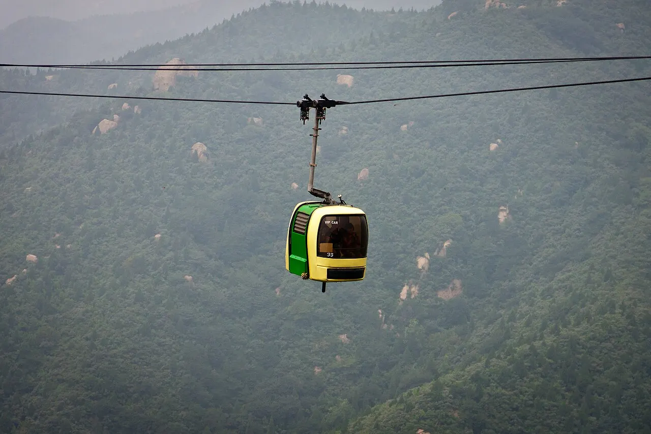 Cabine amarela e verde de teleférico suspensa em cabo sobre colinas cobertas de neblina.