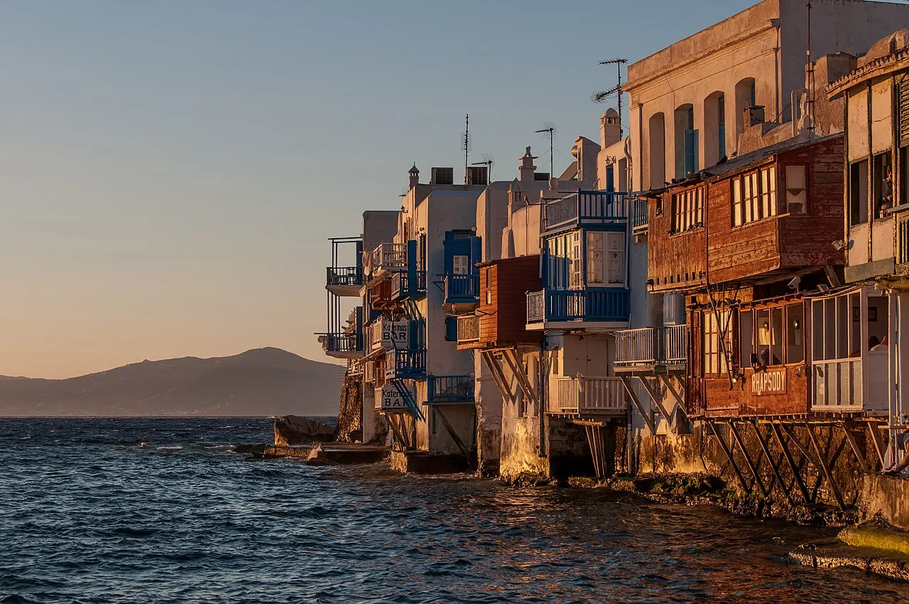 As casas de Little Venice, em Mykonos, com varandas de madeira coloridas debruçadas sobre o mar, iluminadas pela luz dourada do fim da tarde.