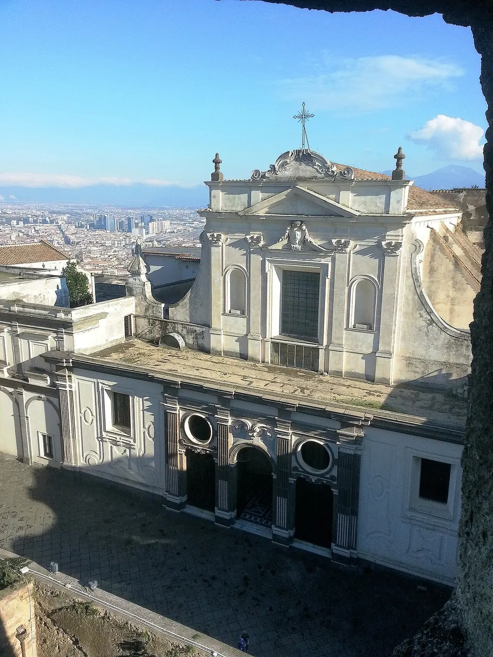 Fachada branca da igreja da Certosa di San Martino, em Nápoles, vista de cima, com o pátio embaixo.