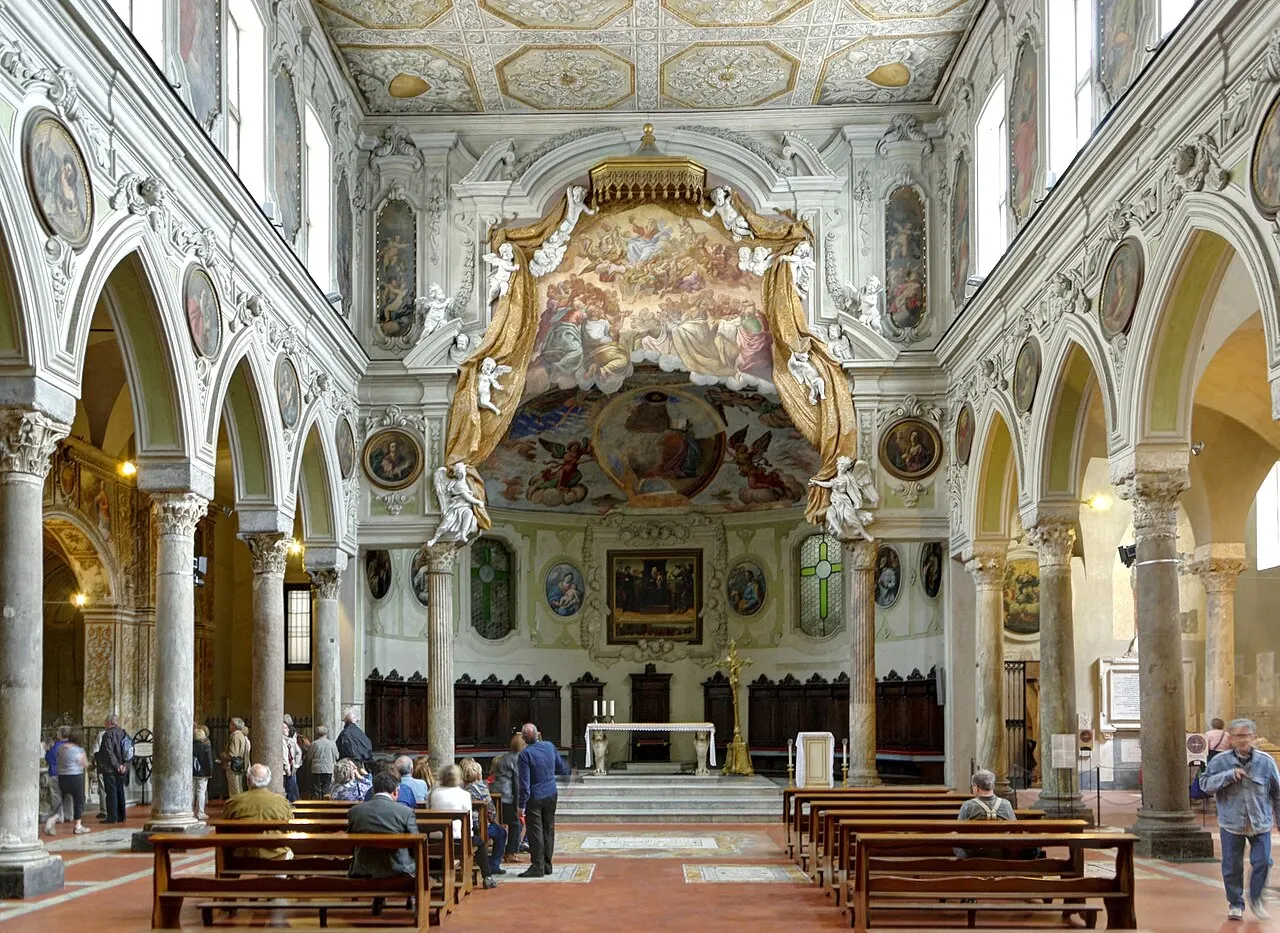Nave com arcos, colunas e altar ao fundo na Basílica de Santa Restituta, dentro do Duomo, com visitantes.