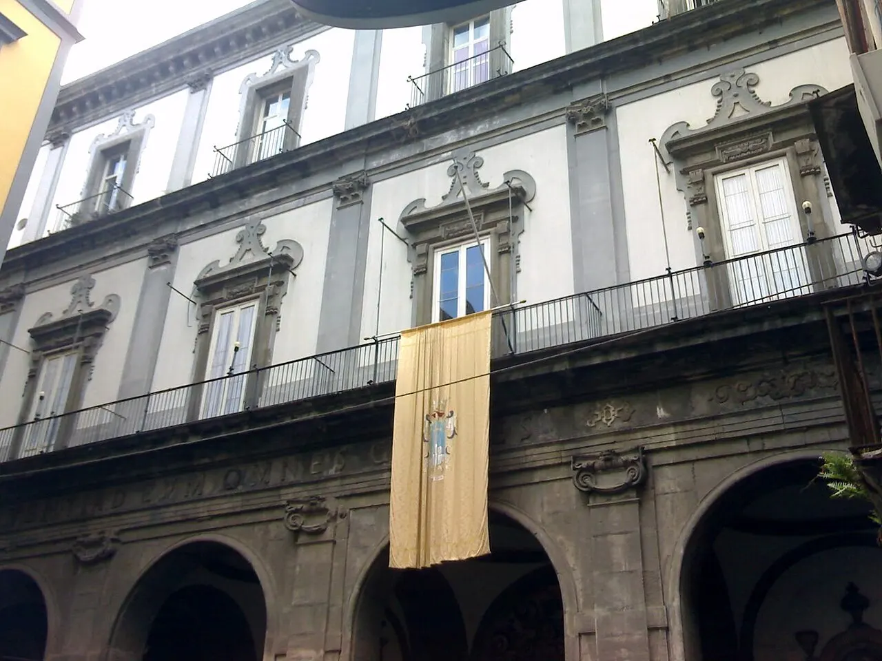 Fachada do Pio Monte della Misericordia, com arcos no térreo, sacadas de ferro e uma faixa pendurada.