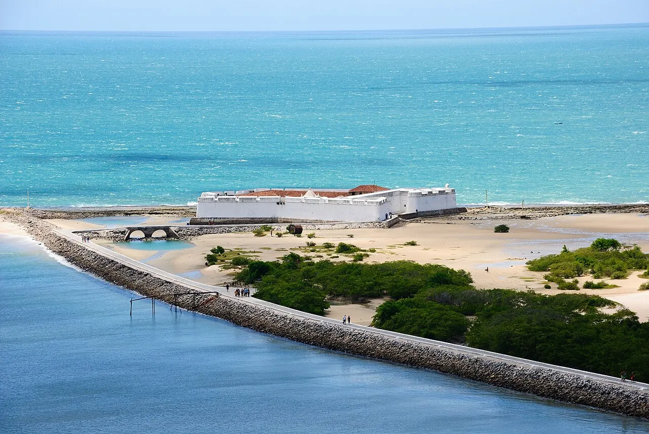 O Forte dos Reis Magos visto do alto, na ponta do recife onde o rio Potengi encontra o mar, com o caminho de pedra que leva até ele e o mar verde-claro em volta.