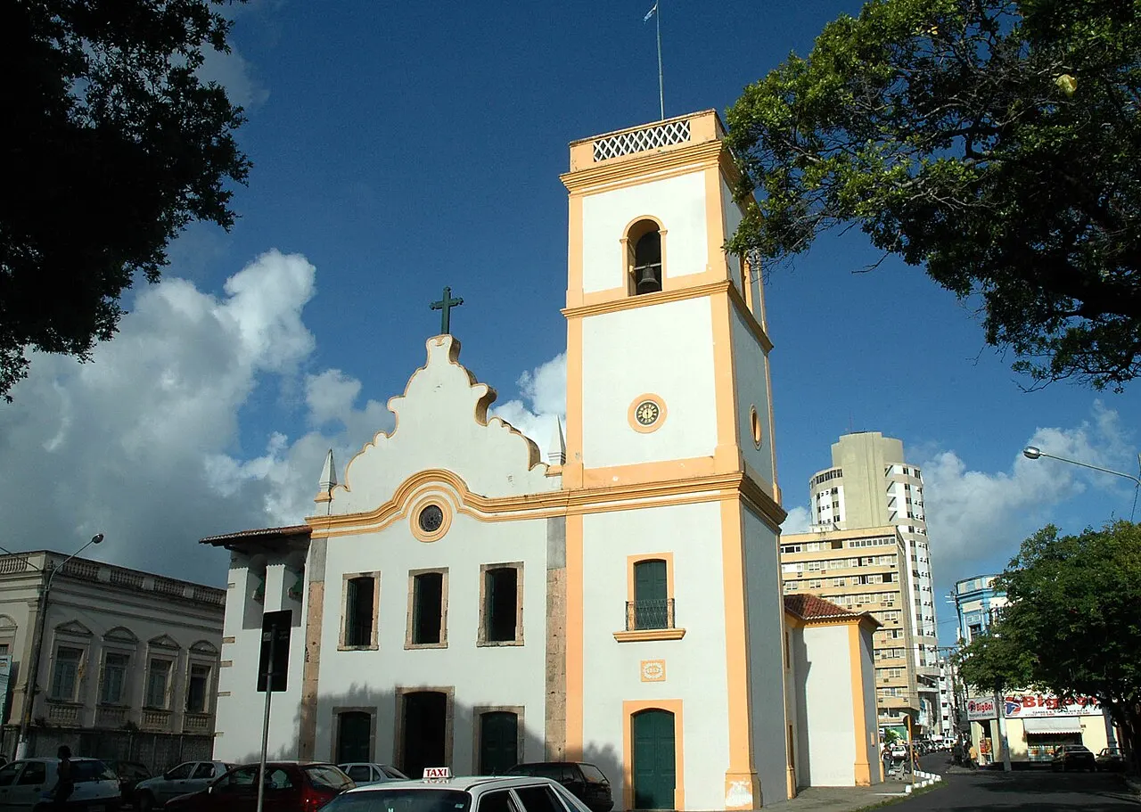 A Igreja Matriz de Nossa Senhora da Apresentação, branca com detalhes amarelos e a torre do sino ao lado, sob céu azul.