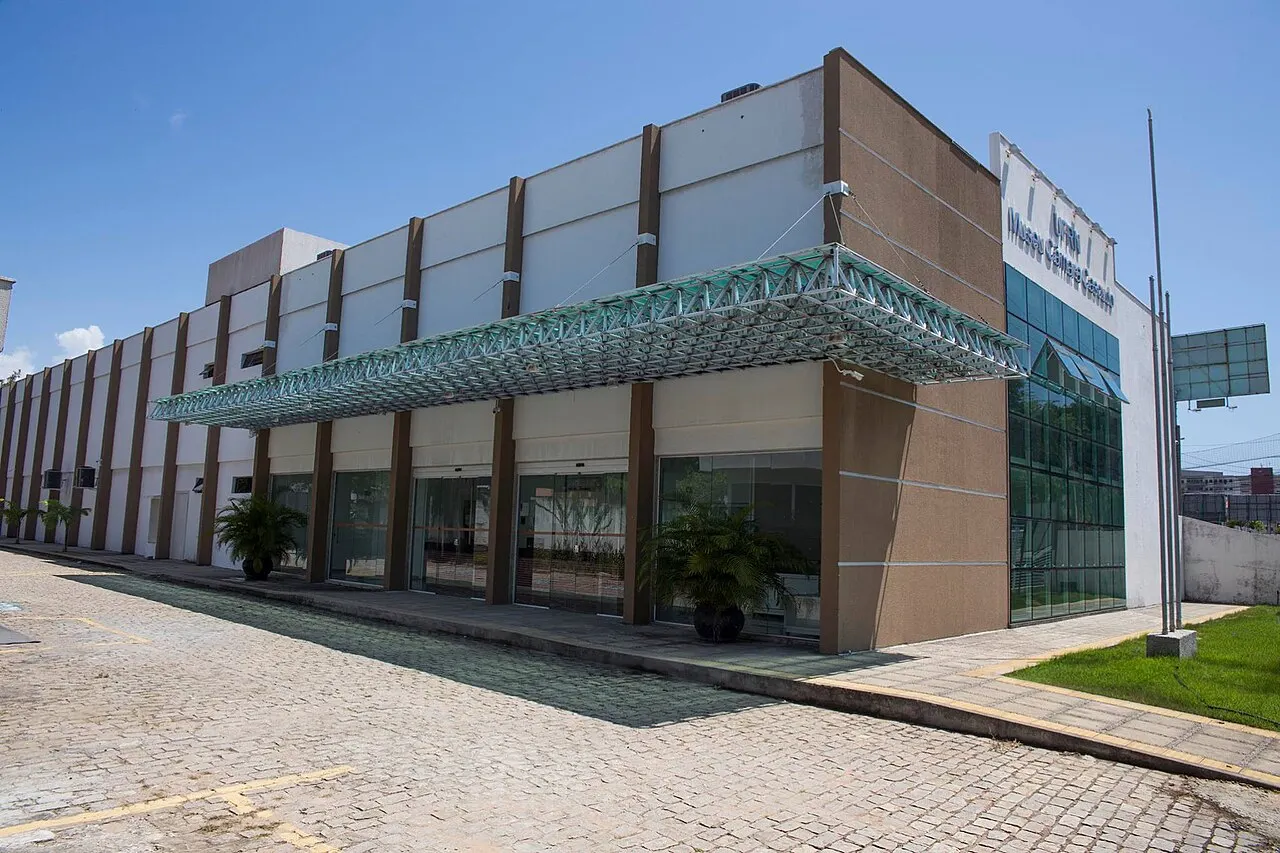 A fachada do prédio de exposições do Museu Câmara Cascudo, de tijolo e vidro, com a marquise sobre a calçada de pedra.