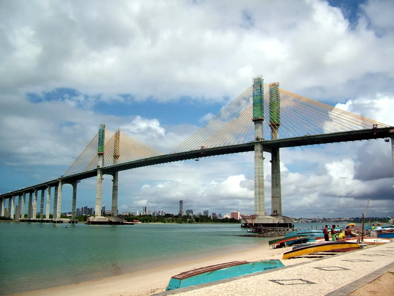 A Ponte Newton Navarro, estaiada, atravessando o rio Potengi, com barcos na margem em primeiro plano.