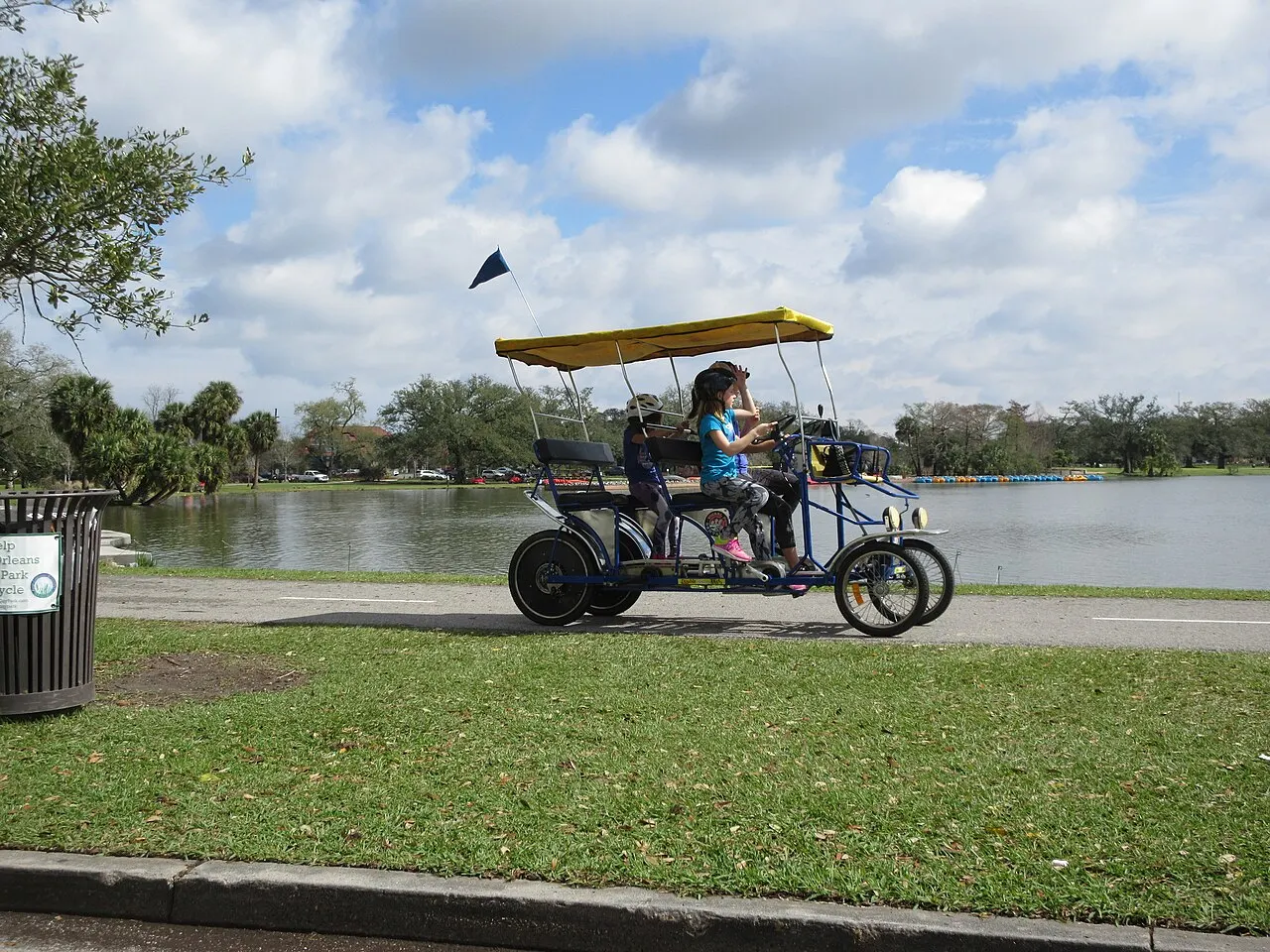 Lagoa do City Park, com gramado em primeiro plano e uma pessoa em um veículo de pedais de passeio.
