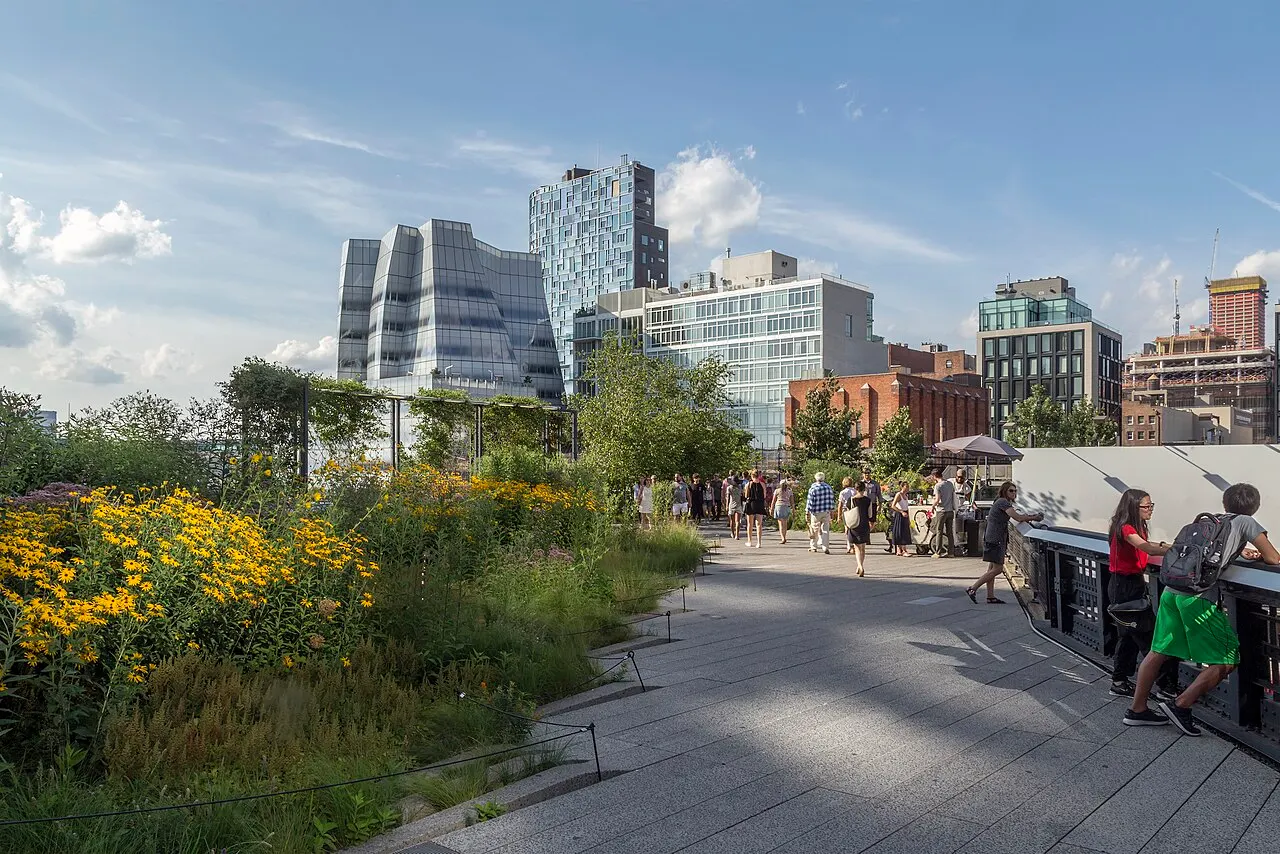 Le chemin du High Line entre des massifs de plantes en fleurs, avec des promeneurs et des immeubles au fond.