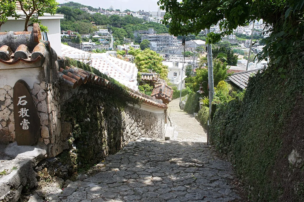 The stone-paved Kinjo-cho slope descending between stone walls, with a red-tiled roof on the left and the city behind.