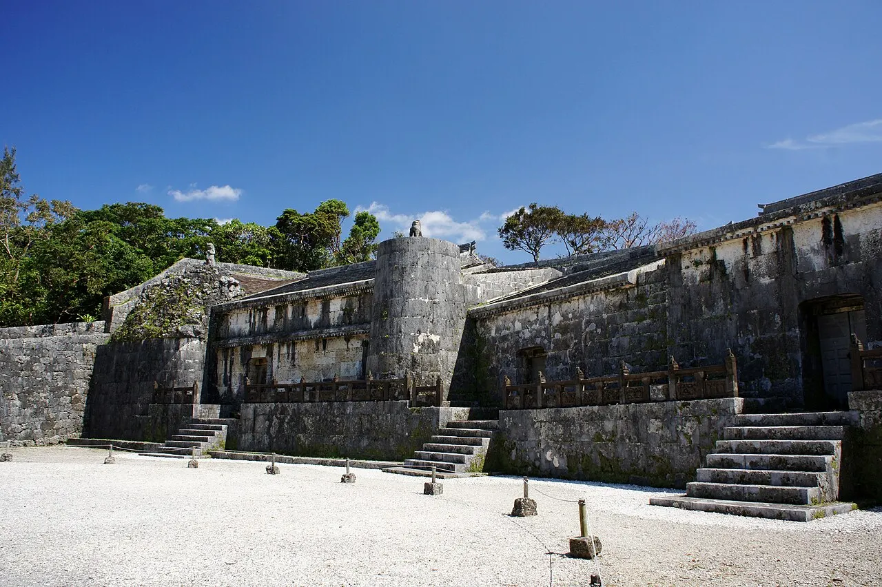 The three chambers of the Tamaudun mausoleum, in darkened limestone, with stone roofs and steps in front of a courtyard of pale gravel.