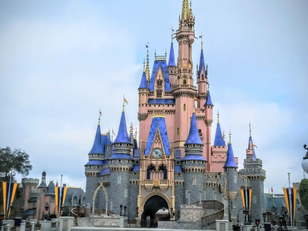 O Castelo da Cinderela, no Magic Kingdom, com paredes rosadas, telhados azuis pontiagudos e uma torre central alta, sob céu claro.