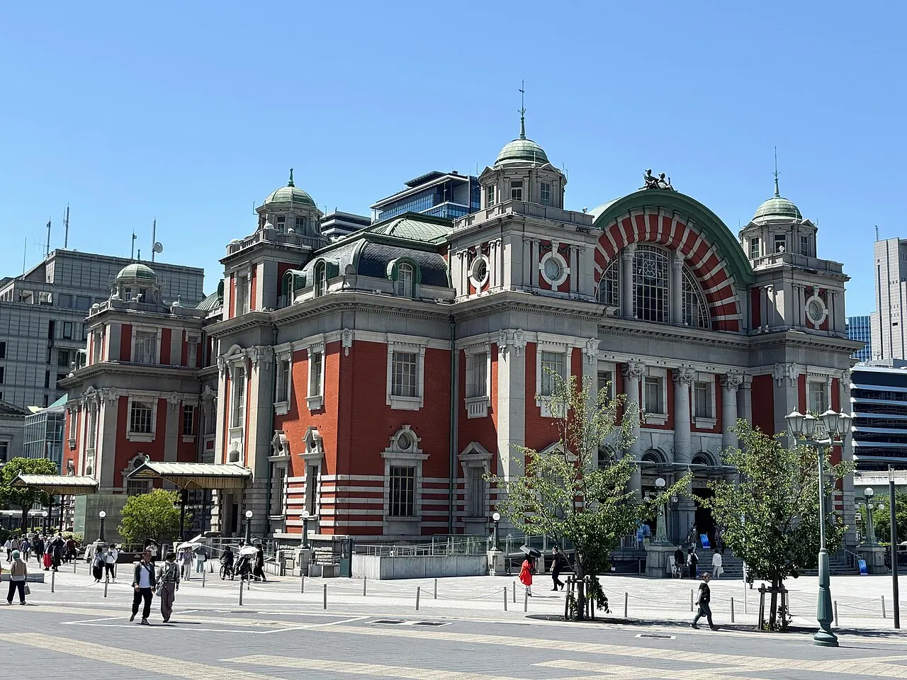 Edifício de tijolo vermelho e pedra clara com cúpulas verdes e uma grande arcada na fachada.